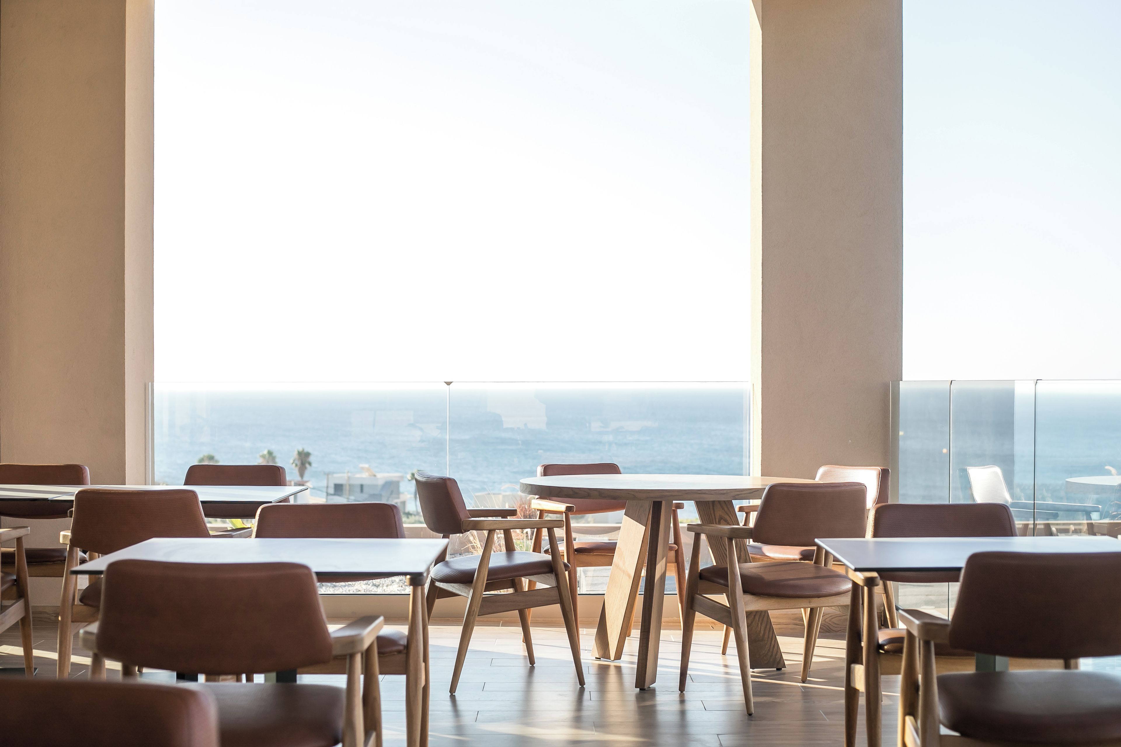 A modern dining area with tables and chairs, large windows, and a view of the ocean.
