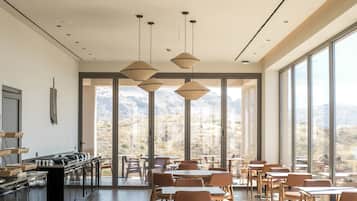 A modern dining area with large windows, a kitchen counter, and pendant lighting.
