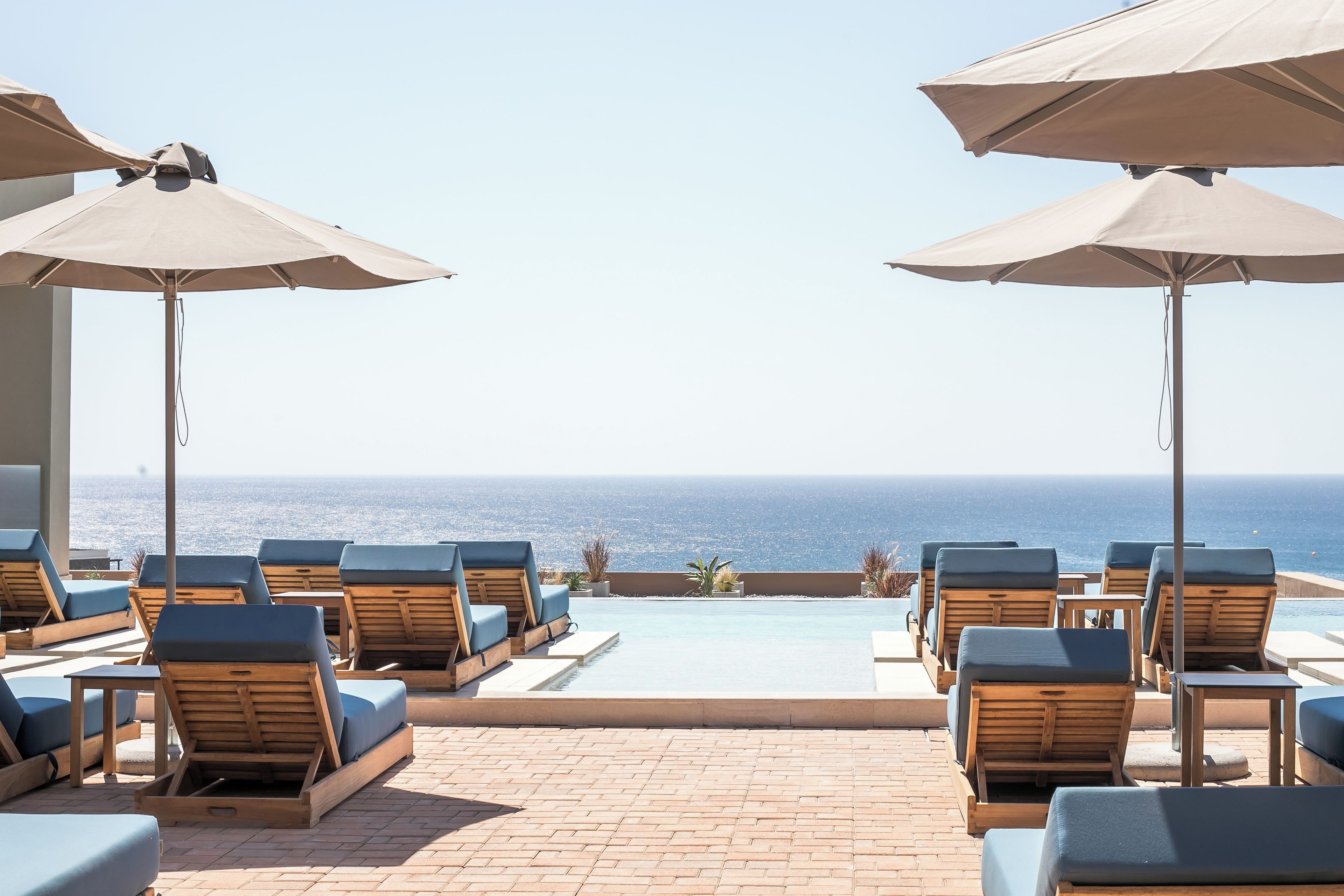 A poolside area with lounge chairs and umbrellas, overlooking the ocean.