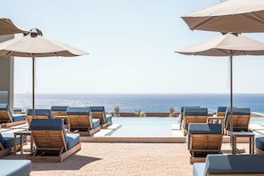 Zona junto a la piscina con sillas de descanso y sombrillas, con vista al océano.