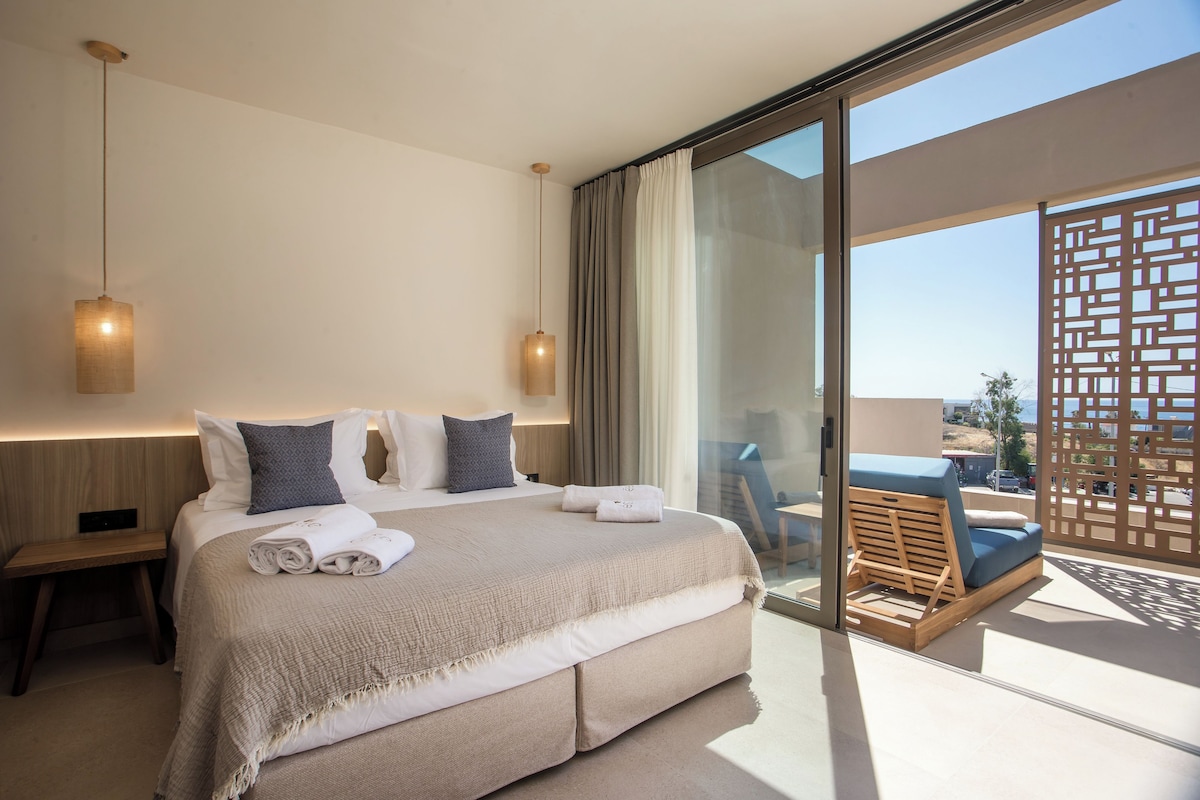 Una habitación de hotel moderna con una cama grande, dos lámparas de noche, un balcón con vistas y una mesita de noche de madera.
