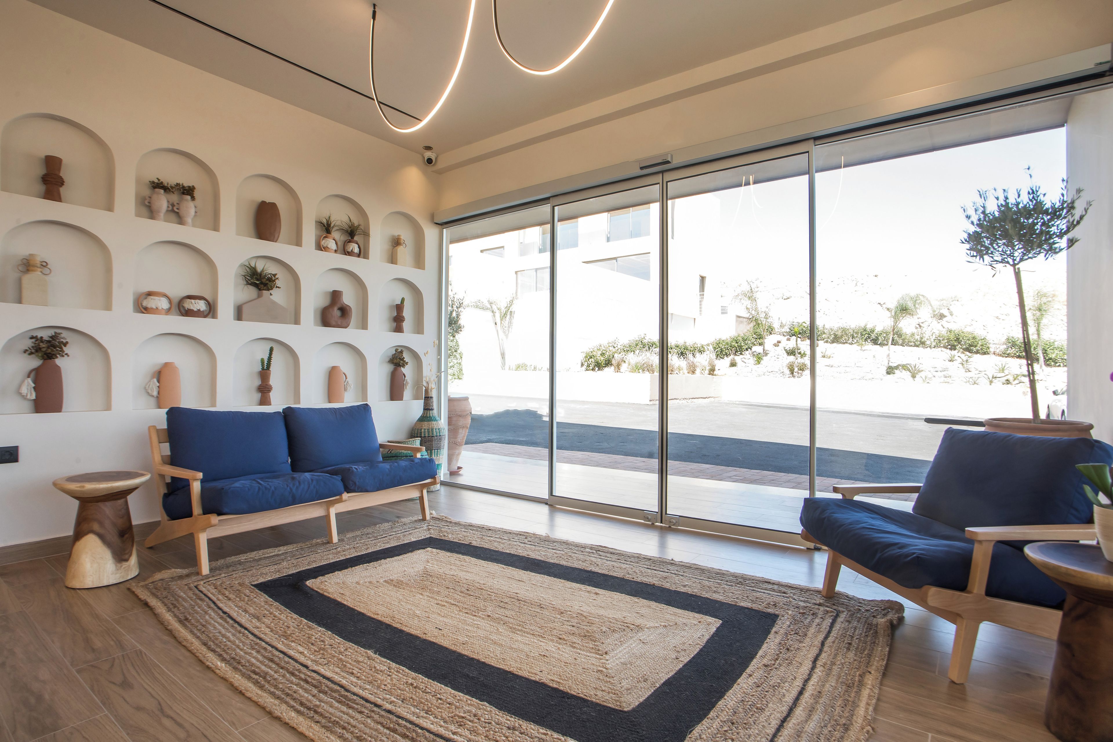 Una sala de estar moderna con un sofá, sillas, un tapete grande y una pared de estantes con objetos decorativos.
