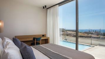 Un dormitori amb un llit gran, un escriptori i vista a una piscina i una platja.