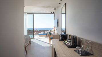 Habitación de hotel moderna con un ventanal grande, una cama, un escritorio con cafetera y un televisor montado en la pared.