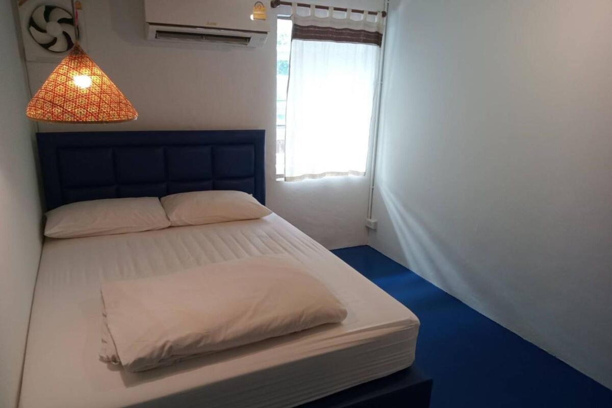A neatly made bed with a blue headboard, a hanging light fixture, and a window with curtains.