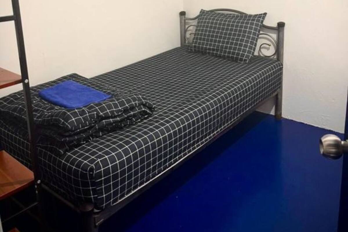 A small, single-bed room with a metal frame, a blue floor, and a white wall.