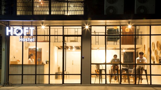 A hostel with a sign reading "HOFT Hostel" and a reception area with a counter and chairs. - Arawana Hoft Hostel (Bangkok)