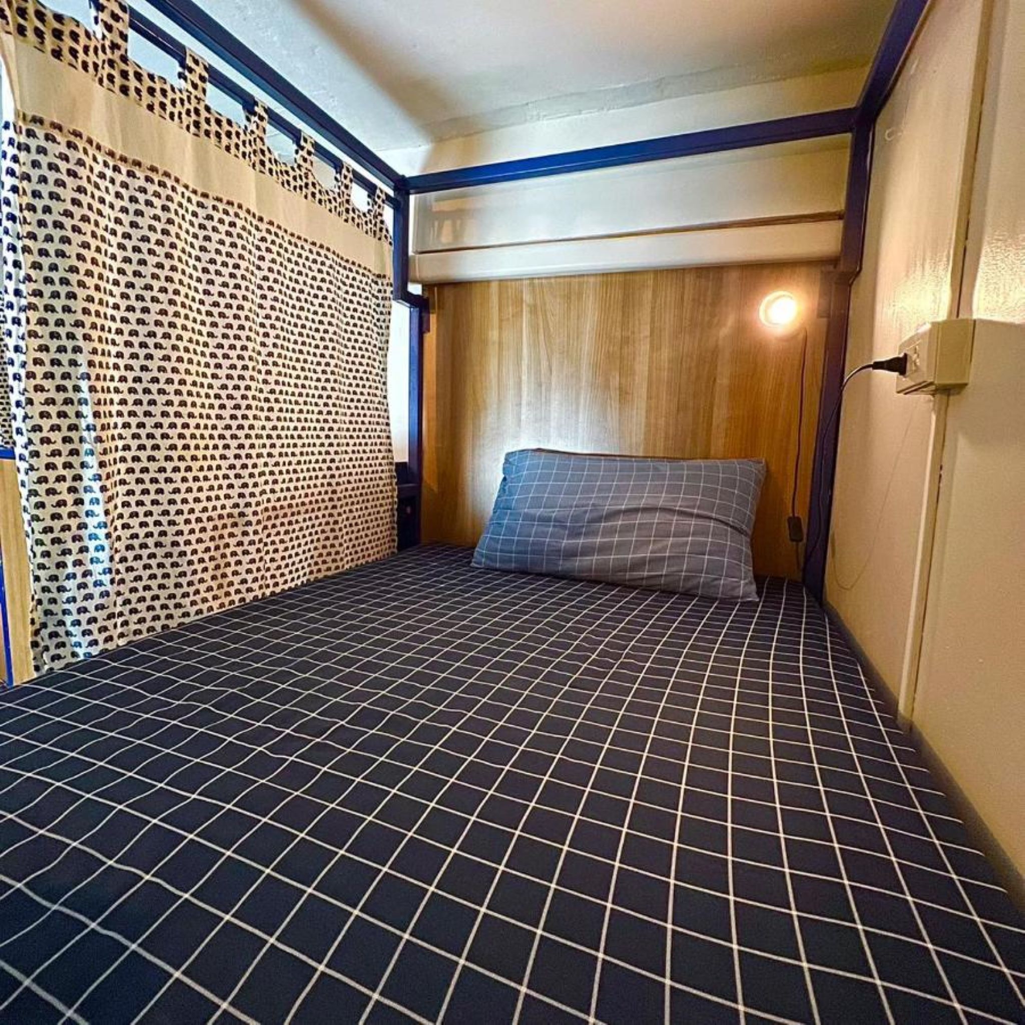 A small, compact room with a bed, a wooden headboard, and a patterned wall.