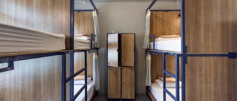 A narrow corridor with bunk beds on either side, a central wardrobe, and a door at the end.