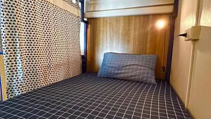 A small, compact room with a bed, a wooden headboard, and a patterned floor. - Arawana Hoft Hostel (Bangkok)