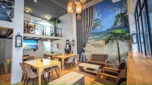 A restaurant with a beach mural, wooden furniture, and a staircase leading to an upper level. - Arawana Hoft Hostel (Bangkok)