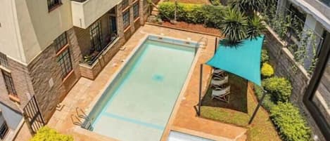 Un edificio de varios pisos con una zona de piscina en la azotea, rodeado de vegetación y un espacio de estar cubierto.