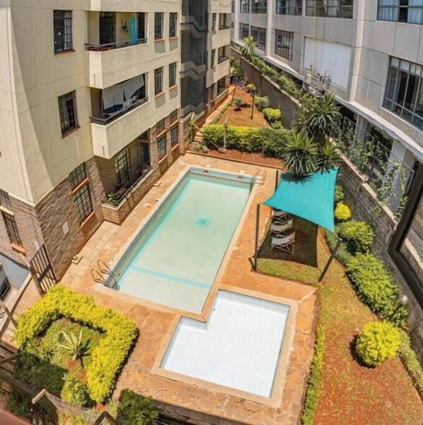 A multi-story building with a rooftop pool area, surrounded by greenery and a covered seating area.