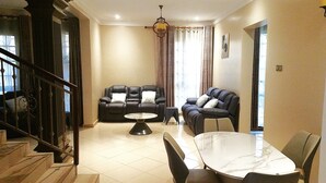 A spacious living area with a sofa set, a dining table, and a staircase. - Serene Retreat with Golf Course, Beach & Wellness Centre Nearby (Akright City)