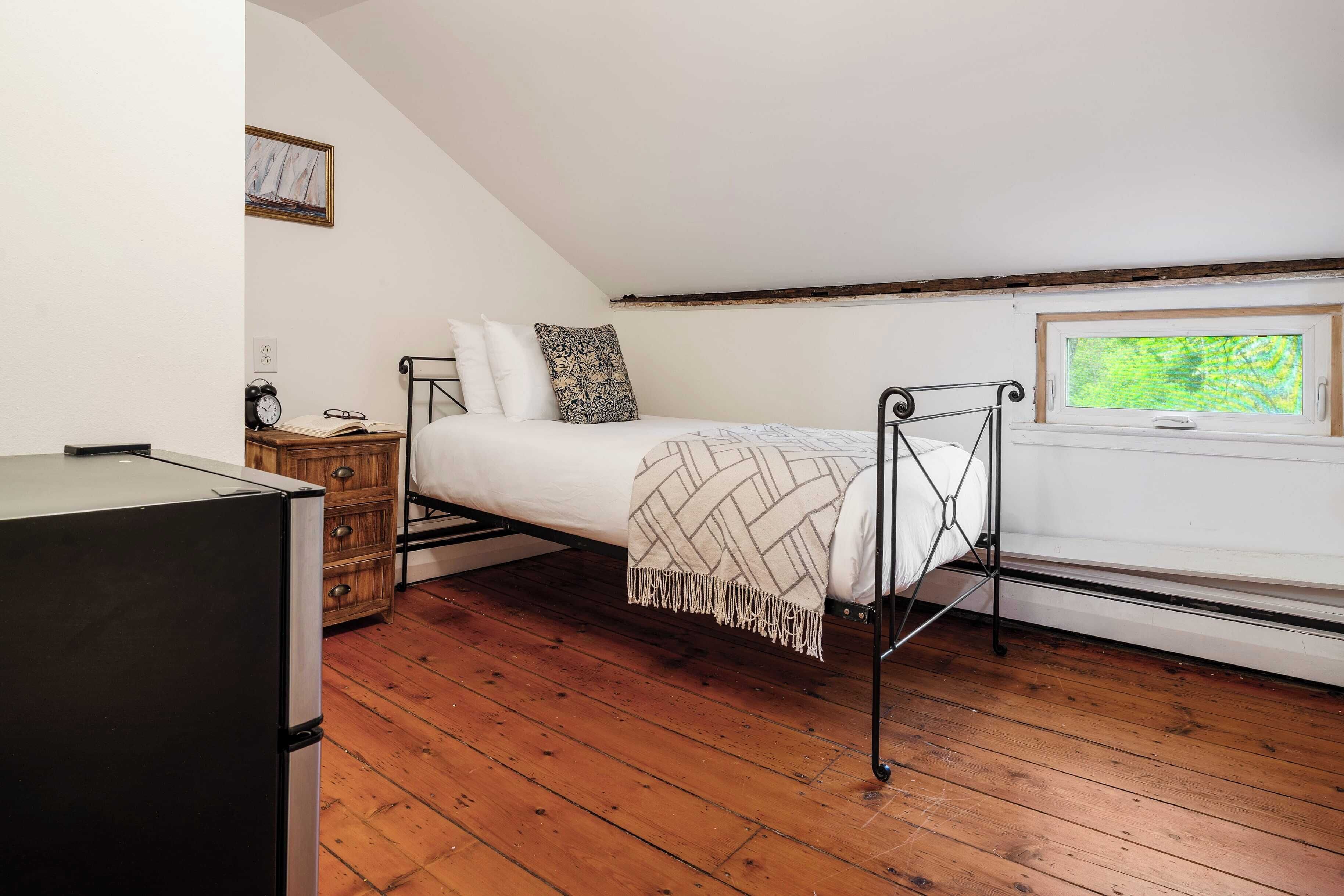 Une chambre avec un lit en mezzanine, une commode, une petite table avec une horloge et une fenêtre donnant sur un paysage verdoyant.
