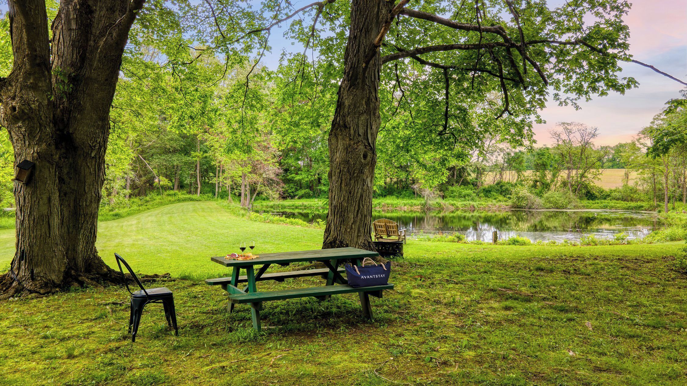 Ein Picknicktisch mit Stühlen und einer Bank, umgeben von Bäumen und einem Teich.