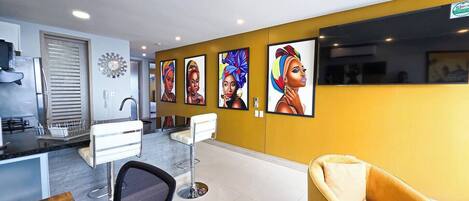 A modern hotel lobby with a yellow accent wall, a reception desk, a bar area, and a seating area with a yellow armchair.