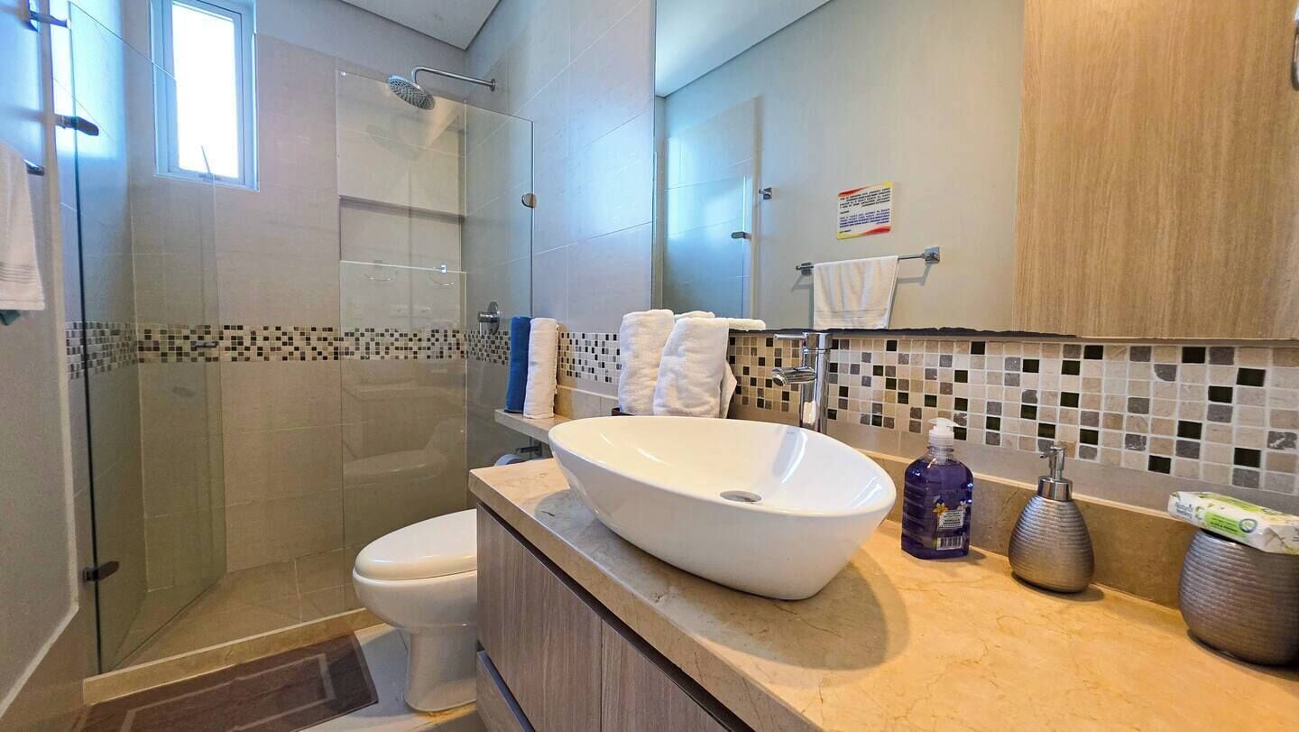 A modern bathroom with a glass-enclosed shower, a white sink, and a tiled backsplash.