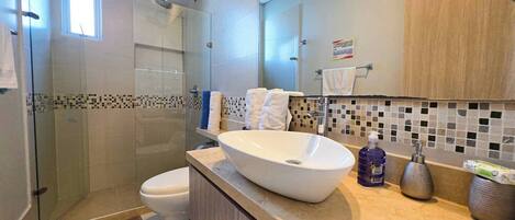 A modern bathroom with a glass-enclosed shower, a white sink, and a tiled backsplash.