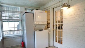 A laundry room with a metal rack, a white refrigerator, a washing machine, and a door with a window.