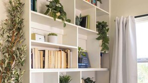 A white bookshelf with multiple shelves, some containing books and others with plants. - Spacious Central & Chic 5BR w/ Luxe Outdoor Living (San Diego)