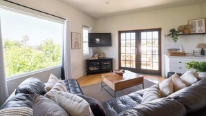 A living room with a leather sofa, a wooden coffee table, and a flat-screen TV. - Spacious Central & Chic 5BR w/ Luxe Outdoor Living (San Diego)
