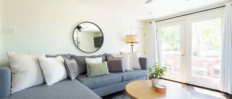 A living room with a grey sofa, a round mirror, a lamp, and a coffee table.