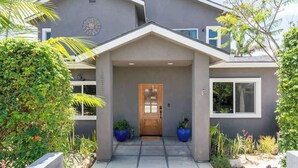 A modern two-story house with a grey facade, a wooden front door, and a small porch area. - Spacious Central & Chic 5BR w/ Luxe Outdoor Living (San Diego)