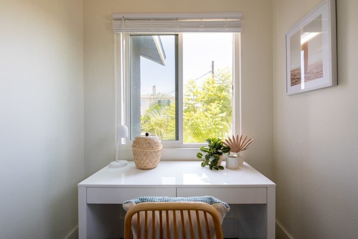 A white desk with a window, a chair, and a small plant on the windowsill.