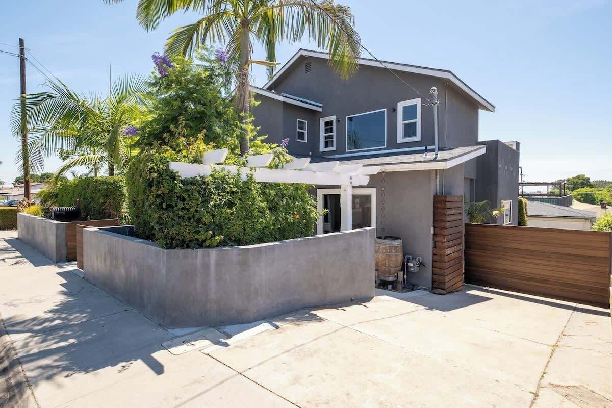 A modern two-story house with a covered patio, a large tree, and a wooden fence.