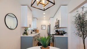A modern kitchen with white cabinets, a dining table with a potted plant, and a large mirror on the wall. - Luxe Boho Retreat by Balboa | Family Sized | Patio (San Diego)