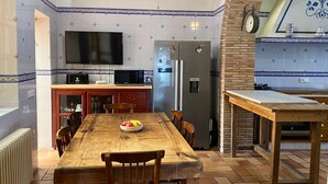 Una cocina con una mesa de madera, sillas, un refrigerador, un microondas y un televisor.