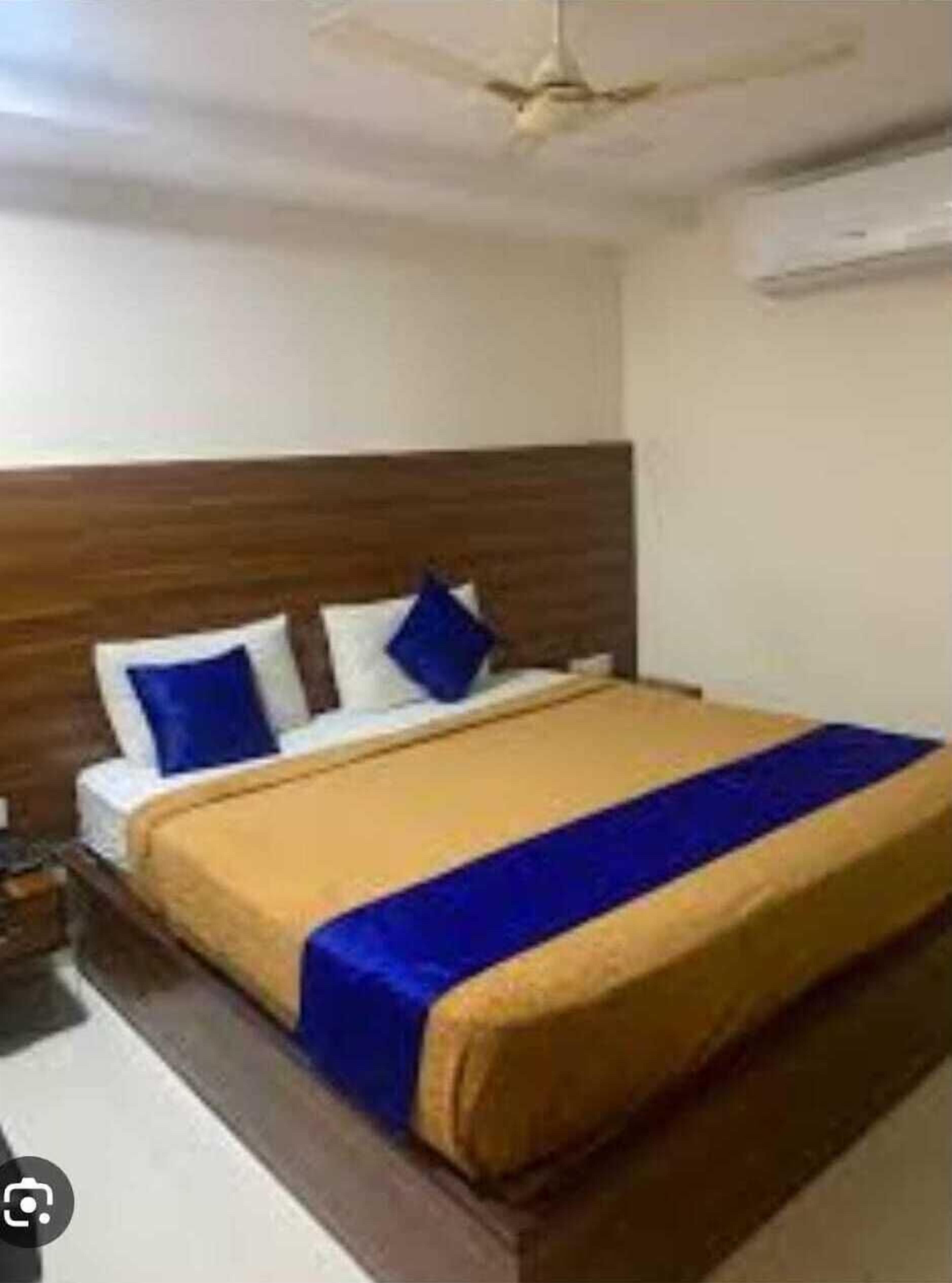 Une chambre à coucher avec une tête de lit en bois, un lit avec des oreillers bleus et blancs, et une couvre-lit bleue et jaune.