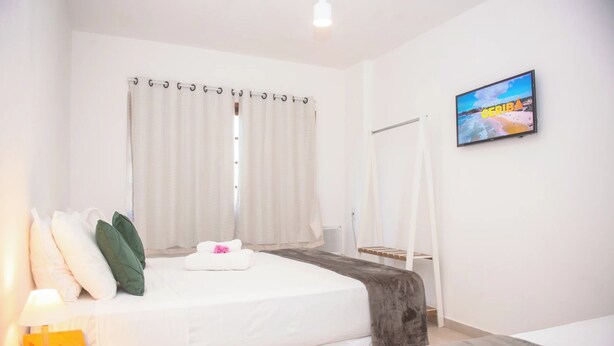 Habitació d'hotel amb un llit, una televisió, una finestra amb cortines i una taula de nit amb una làmpada.