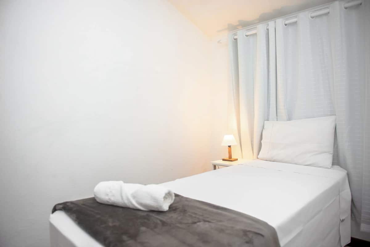 A neatly made bed with a white pillow and a rolled white towel on the side.