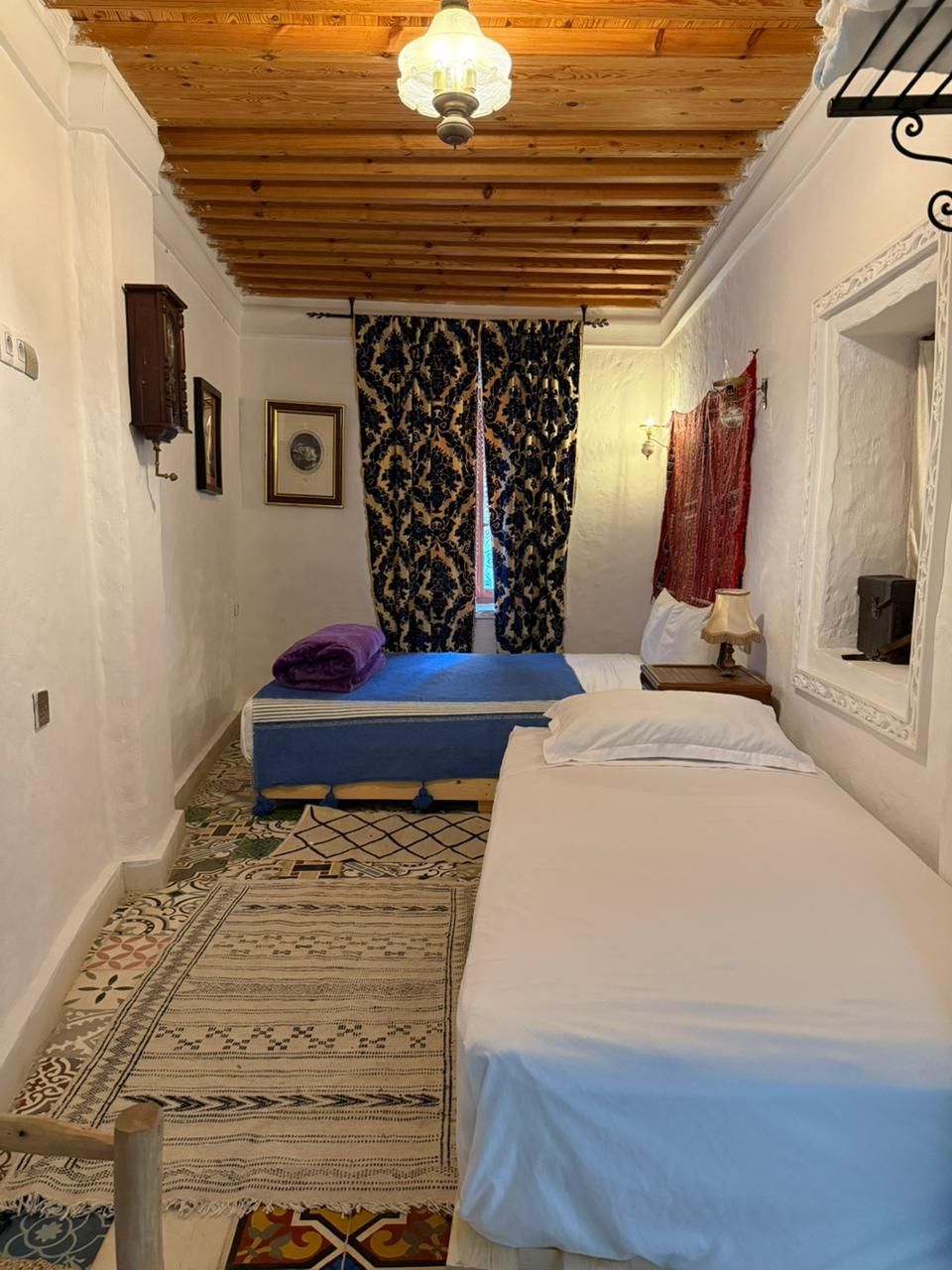 Una habitación con techo de madera, dos camas, cortinas estampadas y una alfombra.