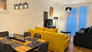 A modern living room with a wooden dining table, yellow sofa, and black armchairs. - Stylish Garden Apartment in Vienna – Peaceful Retreat near Schönbrunn Palace (Wien)