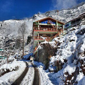 A multi-story building with balconies, situated on a snow-covered slope with a clear sky. - Bohodyssey Hallan (Kullu)