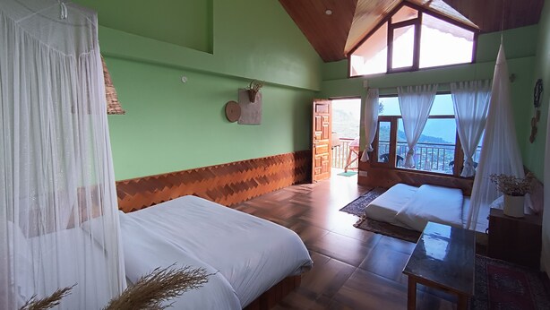 Quarto com duas camas, teto de madeira, vista pela janela e porta para o exterior.
