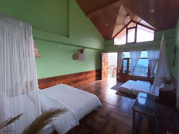 A room with two beds, a wooden ceiling, a view through a window, and a door leading outside. - Bohodyssey Hallan (Kullu)