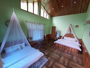 Une chambre avec deux lits, dont l’un est à baldaquin et l’autre non, un plancher en bois, un mur vert et une fenêtre avec des rideaux.