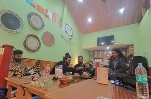 Un groupe de personnes est assis autour d’une table en bois dans une pièce aux murs verts, au plafond en bois et ornée de divers éléments décoratifs.