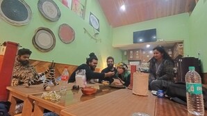 A group of people seated around a wooden table in a room with green walls, wooden ceiling, and various wall decorations. - Bohodyssey Hallan (Kullu)