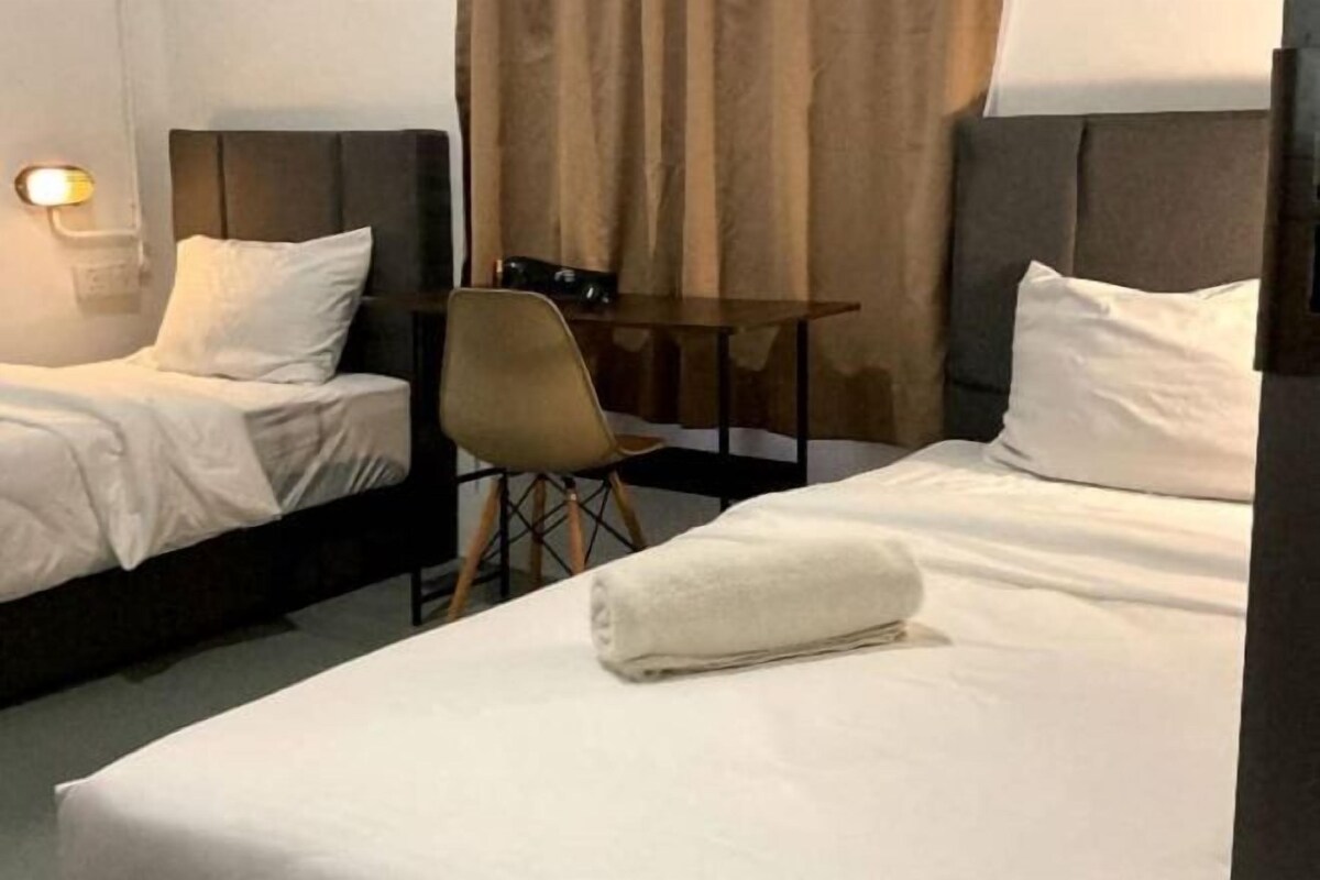 Ein Hotelzimmer mit zwei Betten, einem kleinen Tisch, einem Sessel und einer Lampe.