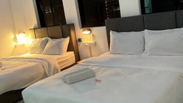 A hotel room with two single beds and one double bed, each with white linens and pillows. There are two bedside tables with lamps, and the room has a modern design with a grey headboard and a large window.