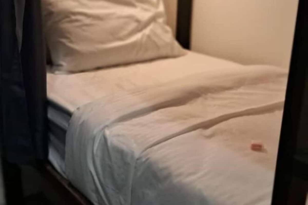 A bed with white bedding, a dark-colored headboard, and a plain wall in the background.