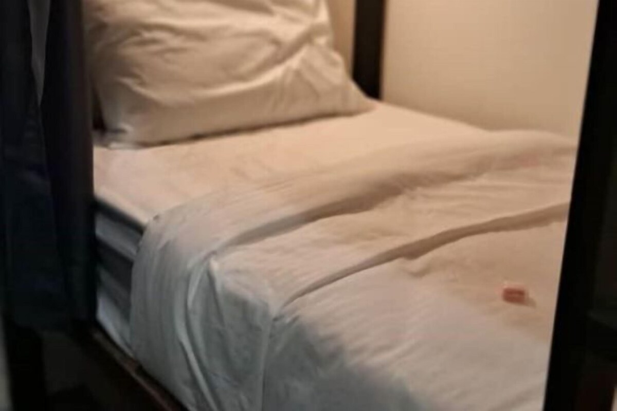 A bed with white bedding, a dark-colored headboard, and a plain wall in the background.