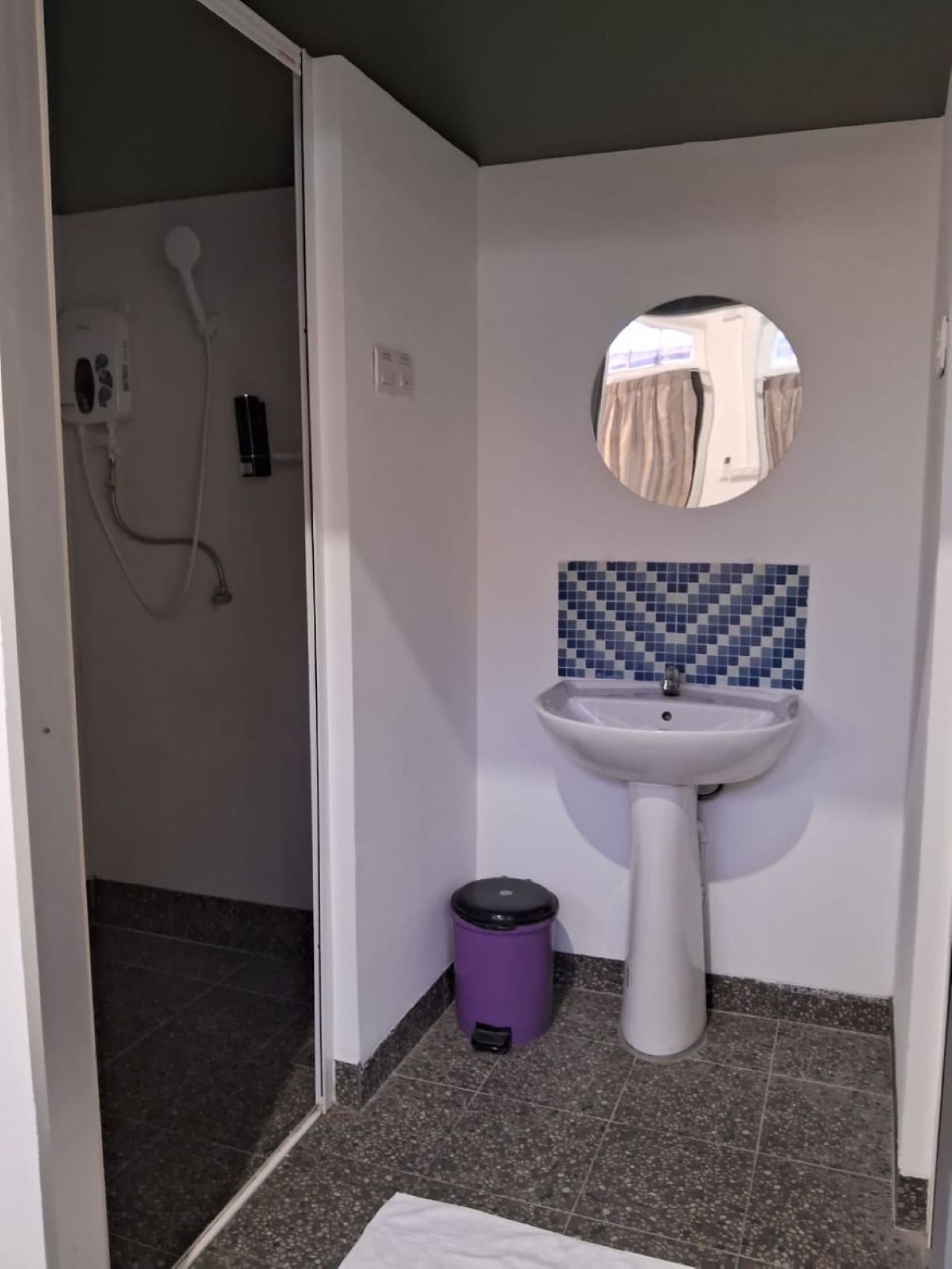 A bathroom with a white pedestal sink, a mirror, and a tiled backsplash.