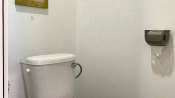 Inodoro blanco con bidé de pared en un baño con encimera de granito y un cuadro en la pared.