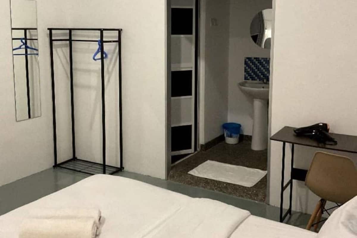 Hotellihuone, jossa on sänky, työpöytä, tuoli, vaatekaappi ja kylpyhuone, joka näkyy avoimesta ovesta.